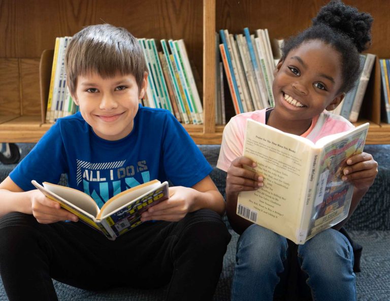 Smiling kids holding books in front of a shelf.