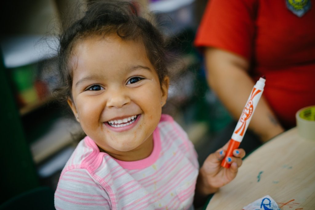 Smiling preschooler holding a marker.