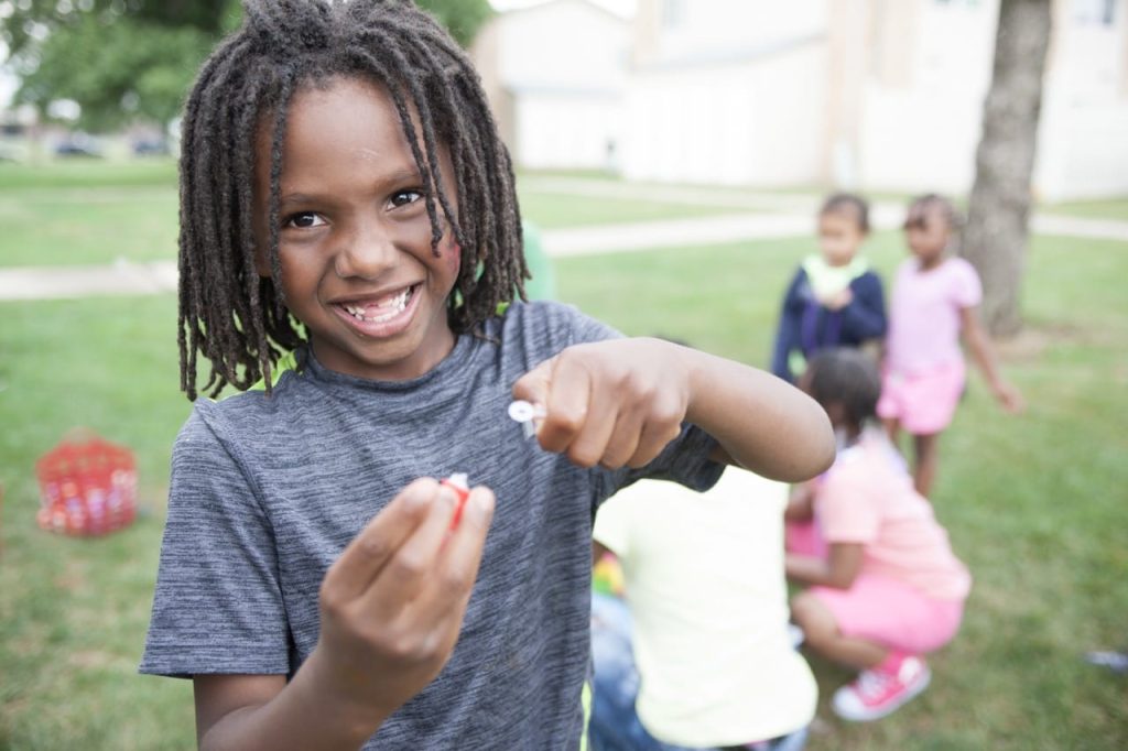 Young boy with dreadlocks holding bubbles wand in his hand.