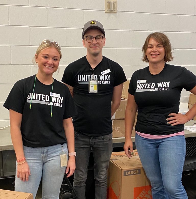 A group of three young smiling employees in black t-shirts and jeans.