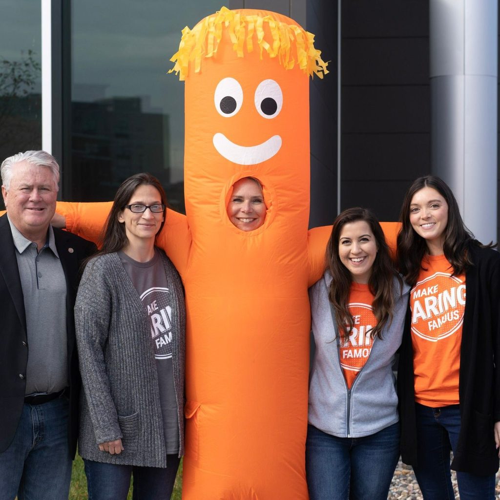 Orange character standing with volunteers.