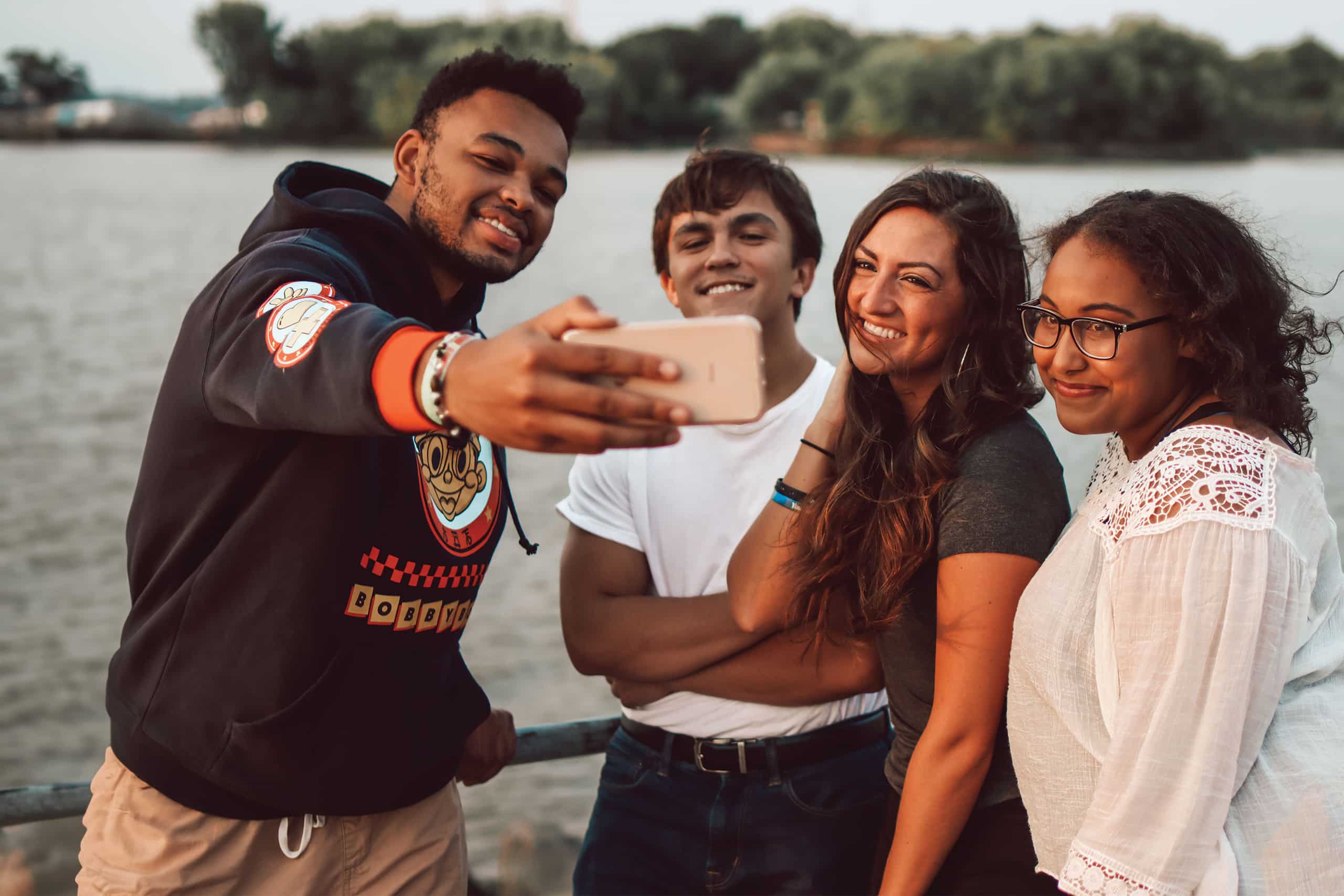 four-young-adults-standing-near-the-water-taking-a-selfie