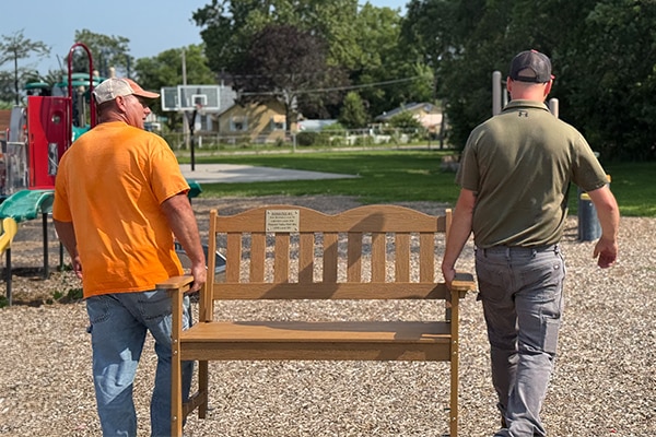 two-men-carrying-a-wooden-bench-across-a-playground