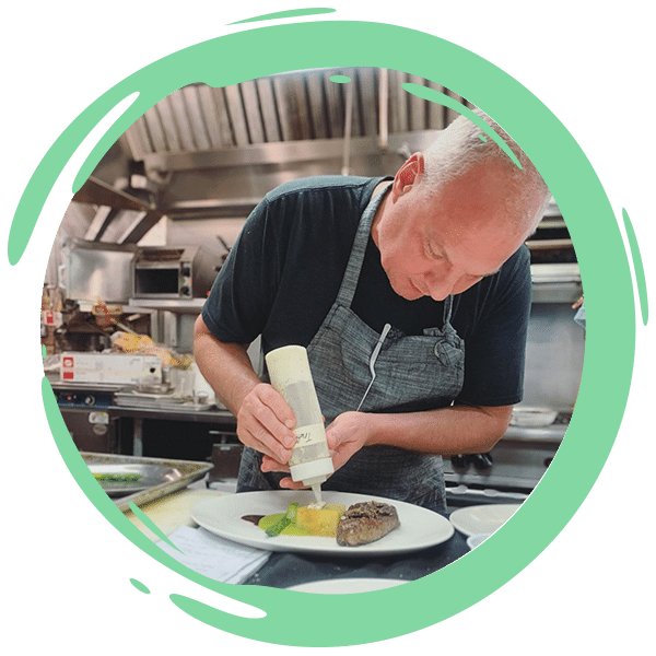 male chef leaning down plating food in a kitchen
