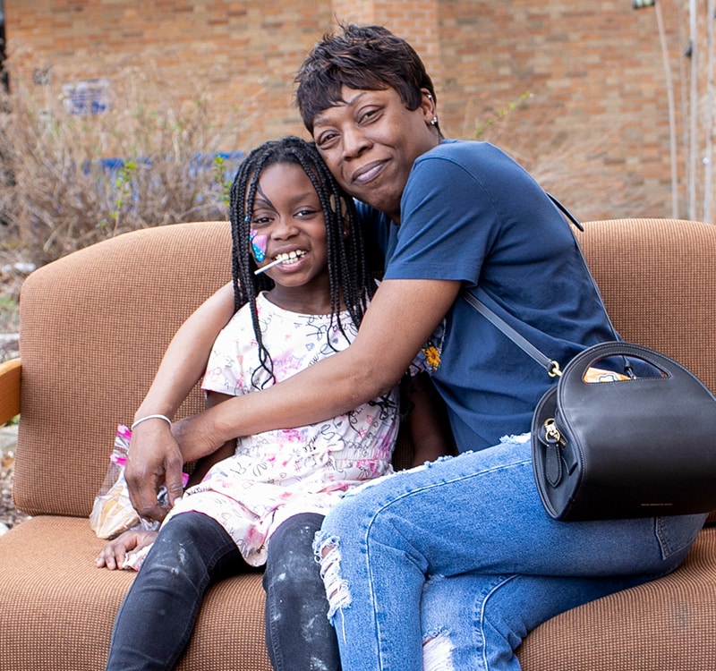 mother with arms around daughter sitting on a couch