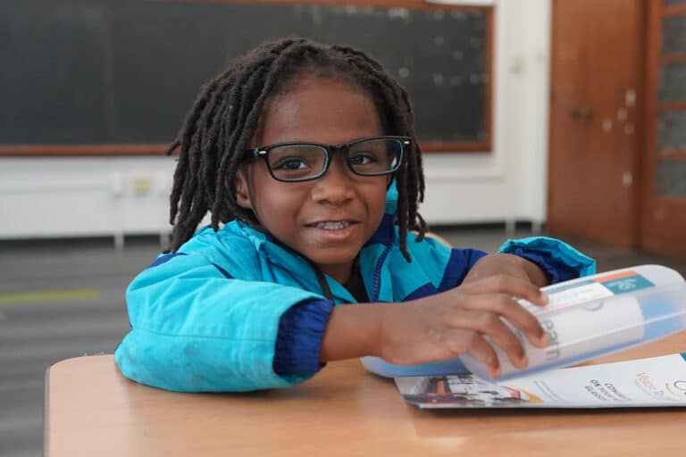 young boy wearing glasses sitting at a table in a classroom