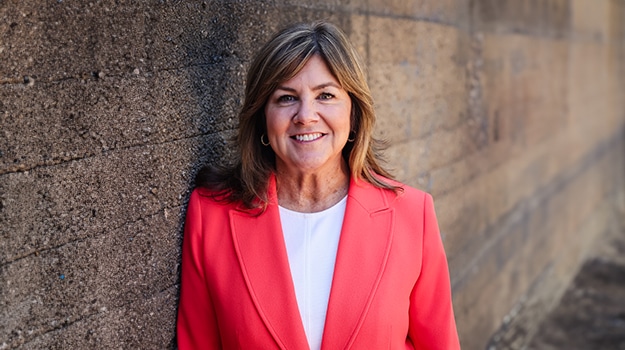 woman in a pink blazer leaning up against a brick wall
