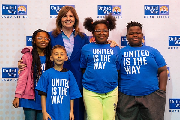 woman standing with a group of 4 elementary age students in blue shirts