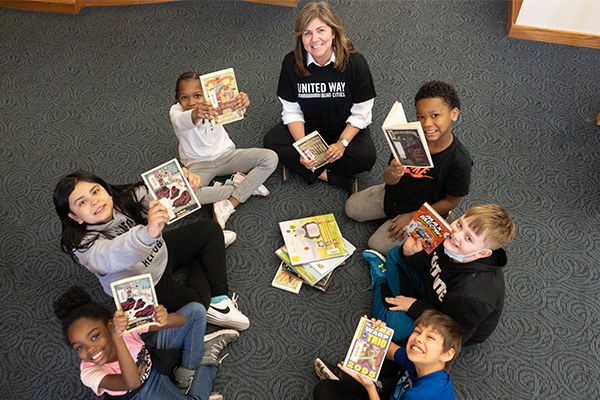 woman sitting in a circle on the floor with a group of kids reading
