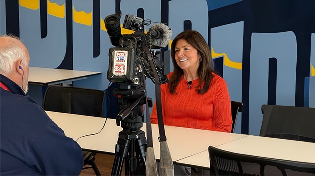 woman in orange sitting for an interview with news camera