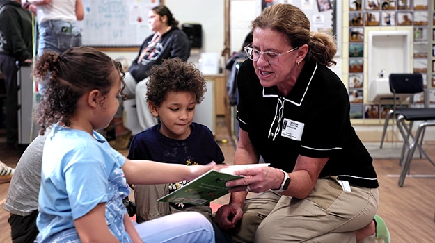 woman sitting down with two kids reading a book