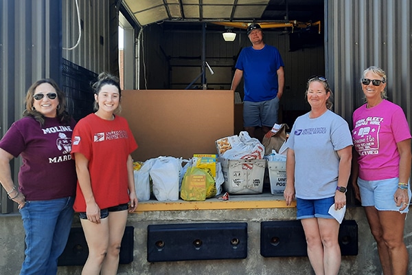 five people standing near a loading dock with boxes and bags of donated food