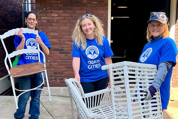 three women in blue shirts outside moving some shite chairs