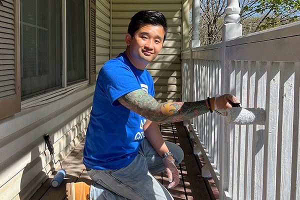 man in a blue shirt kneeling down painting a white railing