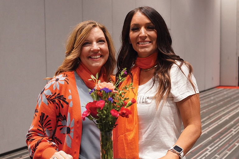 two women standing together wearing orange scarfs