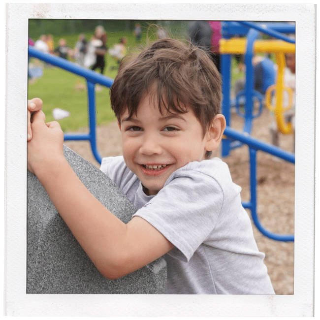 young boy holding onto rock climbing wall smiling