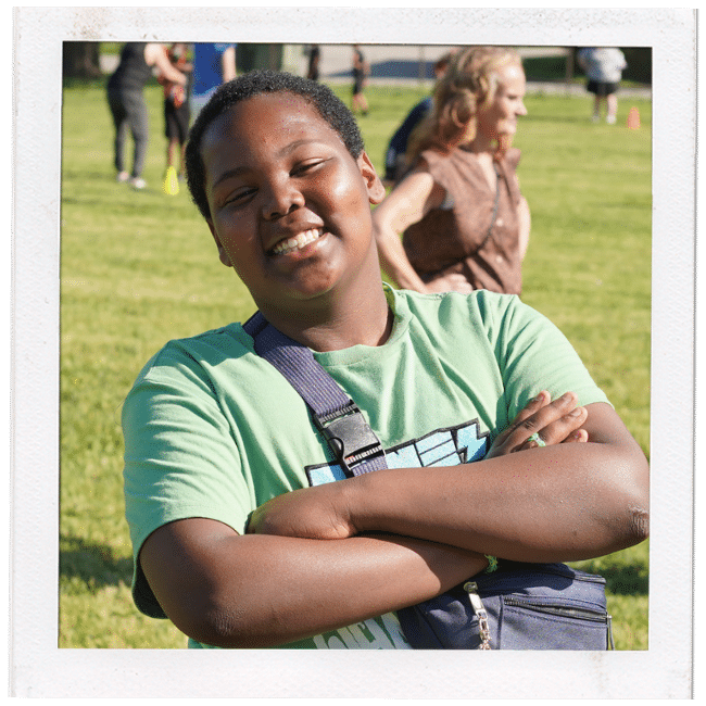 boy in a green shirt with arms crossed smiling