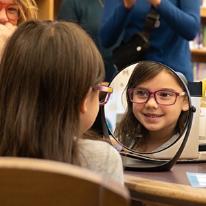 young girl with glasses looking into a mirror