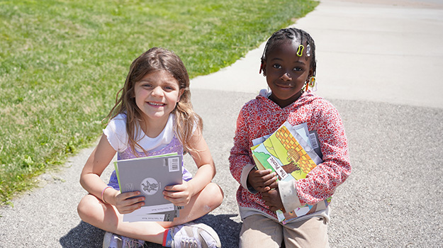 two young girls holding books sitting outside