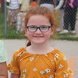 young girl in an orange shirt and glasses smiling